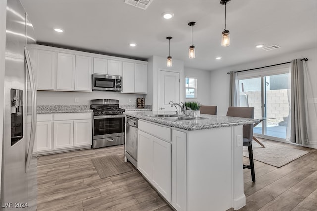 kitchen with a kitchen island with sink, stainless steel appliances, white cabinets, light stone counters, and light hardwood / wood-style floors