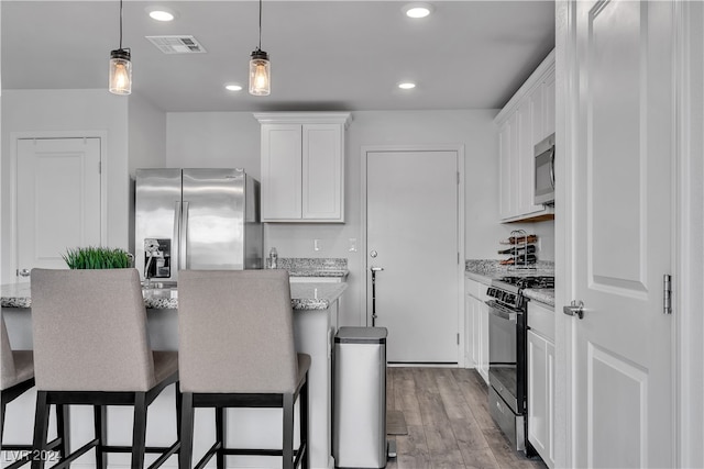 kitchen with light stone countertops, appliances with stainless steel finishes, light wood-type flooring, and white cabinets