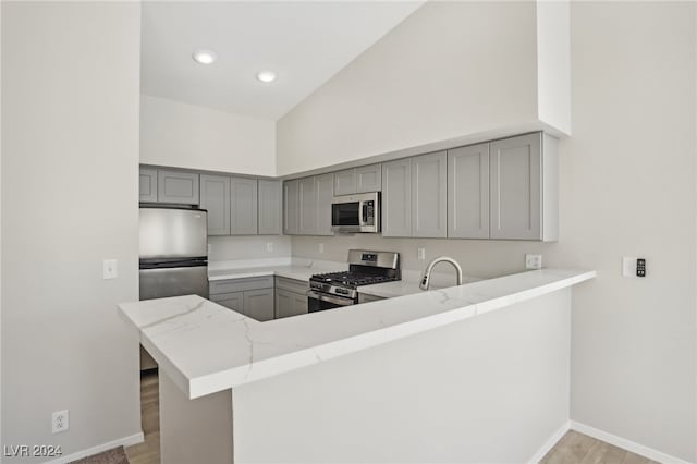 kitchen with kitchen peninsula, stainless steel appliances, light wood-type flooring, gray cabinets, and high vaulted ceiling