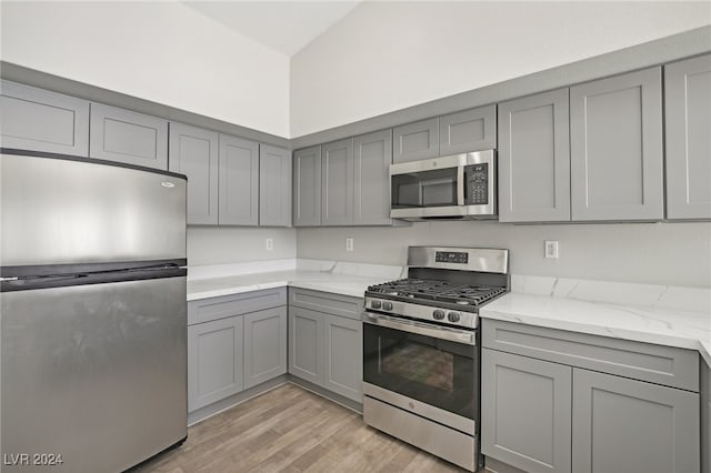 kitchen featuring gray cabinetry, light hardwood / wood-style floors, stainless steel appliances, and light stone counters