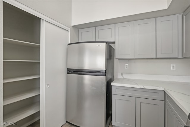 kitchen with gray cabinets, light stone countertops, and stainless steel refrigerator