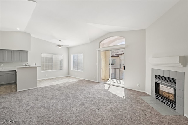 unfurnished living room featuring sink, a tile fireplace, light carpet, ceiling fan, and lofted ceiling