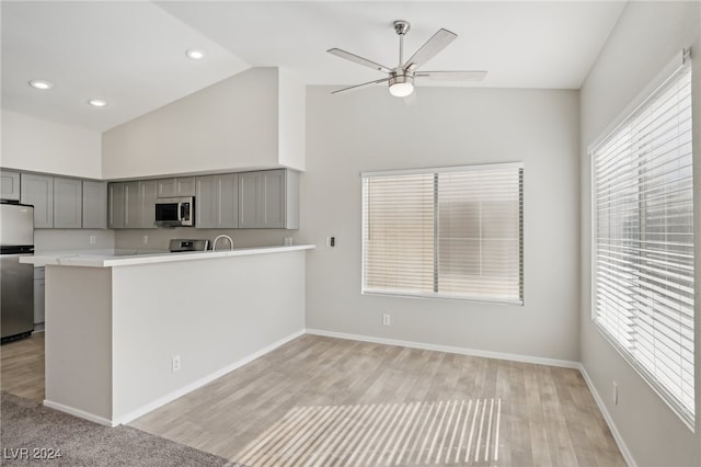 kitchen with appliances with stainless steel finishes, kitchen peninsula, light wood-type flooring, and vaulted ceiling