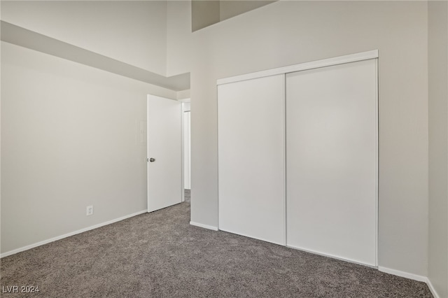 unfurnished bedroom featuring a high ceiling, dark colored carpet, and a closet