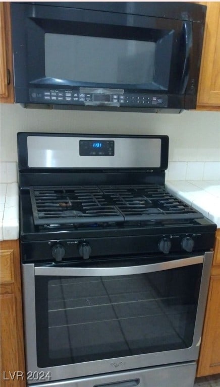 interior details featuring tile countertops, stainless steel range with gas stovetop, and decorative backsplash