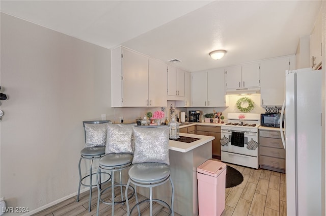 kitchen featuring kitchen peninsula, white cabinets, a breakfast bar, light hardwood / wood-style flooring, and white appliances