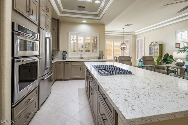 kitchen with a raised ceiling, sink, decorative backsplash, a kitchen island, and stainless steel appliances