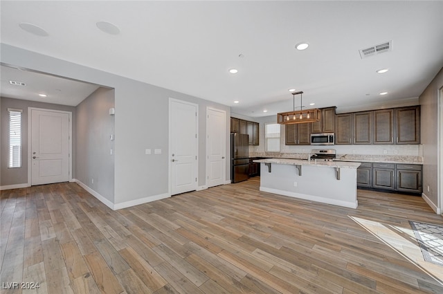 kitchen featuring appliances with stainless steel finishes, an island with sink, a breakfast bar, hanging light fixtures, and light hardwood / wood-style flooring