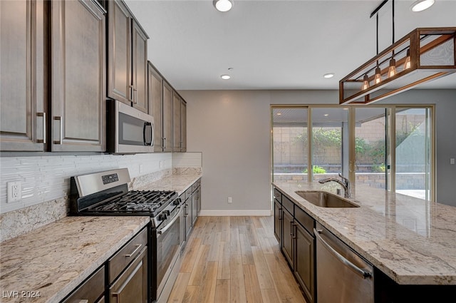 kitchen featuring light stone countertops, stainless steel appliances, sink, light hardwood / wood-style floors, and decorative light fixtures