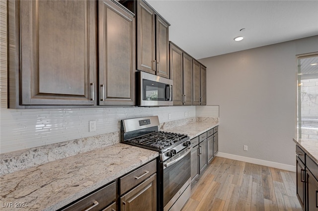 kitchen with dark brown cabinets, backsplash, appliances with stainless steel finishes, light stone countertops, and light hardwood / wood-style floors