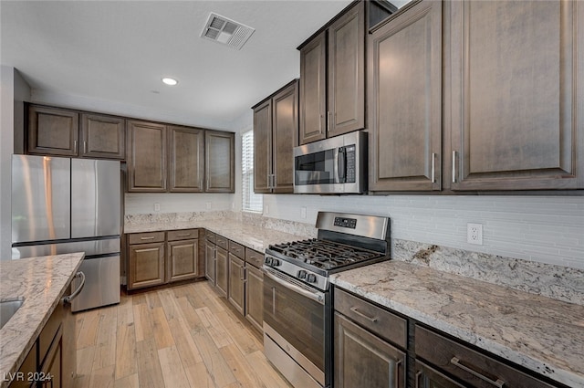 kitchen with dark brown cabinetry, light stone counters, appliances with stainless steel finishes, and light hardwood / wood-style flooring