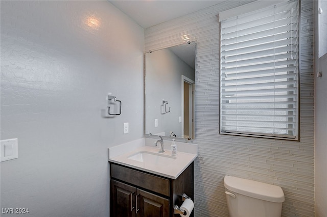 bathroom featuring toilet, vanity, and tile walls