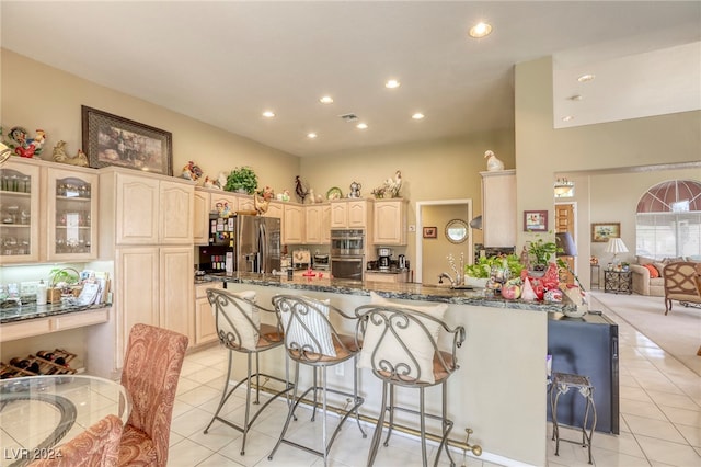 kitchen with kitchen peninsula, light tile patterned floors, a kitchen breakfast bar, dark stone counters, and stainless steel appliances