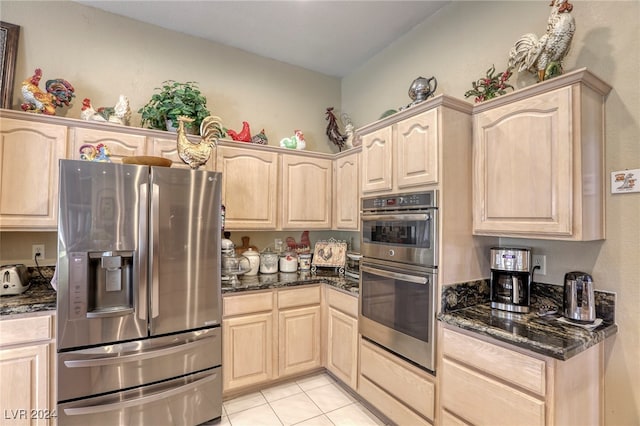 kitchen featuring light brown cabinets, stainless steel appliances, light tile patterned floors, and dark stone counters