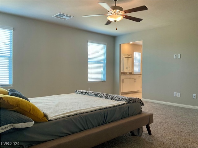 carpeted bedroom featuring multiple windows, ensuite bath, sink, and ceiling fan