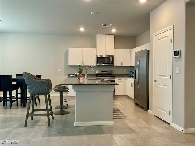 kitchen with white cabinets, a breakfast bar area, dark stone countertops, sink, and stainless steel appliances