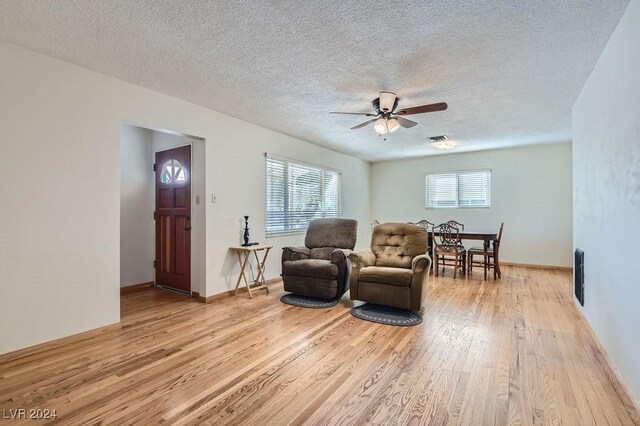 living room with ceiling fan, plenty of natural light, light wood-type flooring, and a textured ceiling