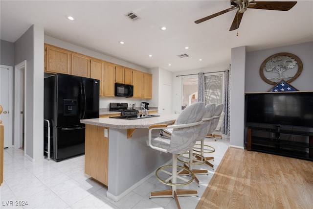 kitchen with light brown cabinetry, black appliances, a kitchen island with sink, and a kitchen bar