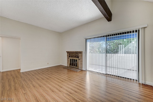 unfurnished living room featuring light hardwood / wood-style flooring, a textured ceiling, beam ceiling, and a fireplace