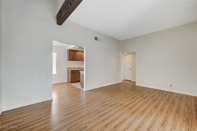 unfurnished living room with beamed ceiling, a textured ceiling, and light wood-type flooring