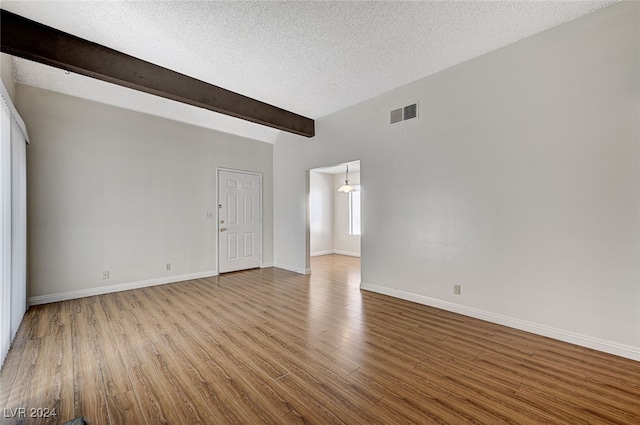 spare room featuring beamed ceiling, a textured ceiling, and light wood-type flooring