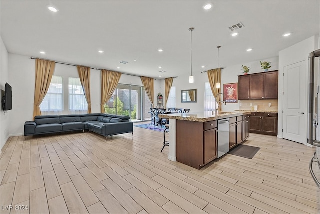 kitchen with light wood-type flooring, an island with sink, dark brown cabinetry, decorative light fixtures, and stainless steel dishwasher