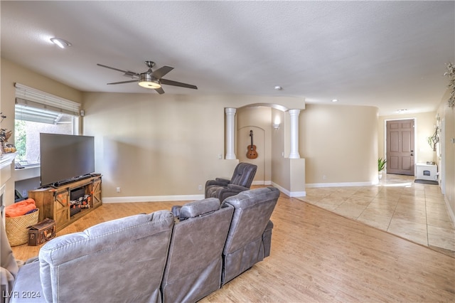 living room with a textured ceiling, light hardwood / wood-style flooring, ceiling fan, and decorative columns