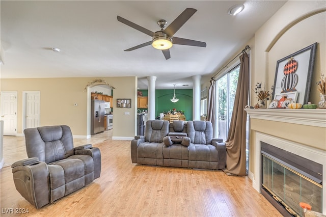 living room with light hardwood / wood-style flooring, ceiling fan, and decorative columns