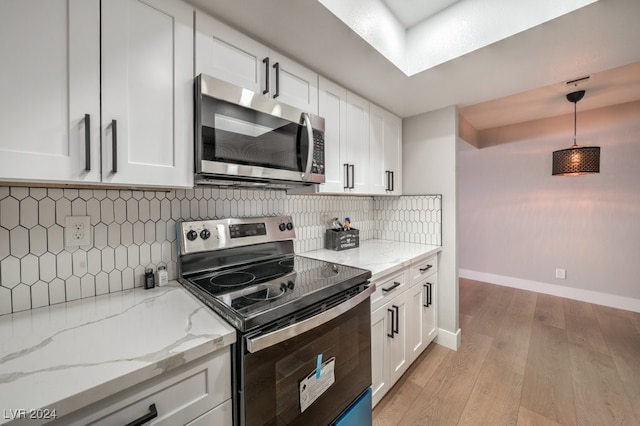 kitchen with appliances with stainless steel finishes, white cabinetry, decorative light fixtures, decorative backsplash, and light hardwood / wood-style flooring