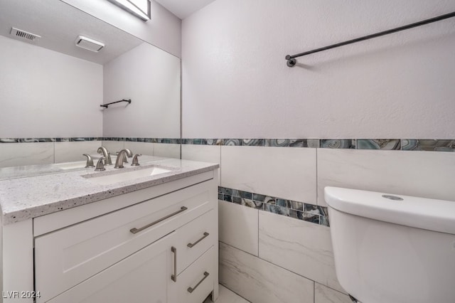 bathroom featuring toilet, vanity, and tile walls