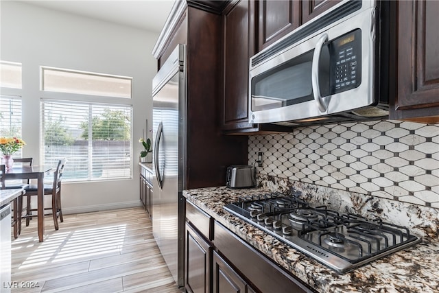 kitchen with appliances with stainless steel finishes, backsplash, light hardwood / wood-style floors, dark brown cabinetry, and light stone counters