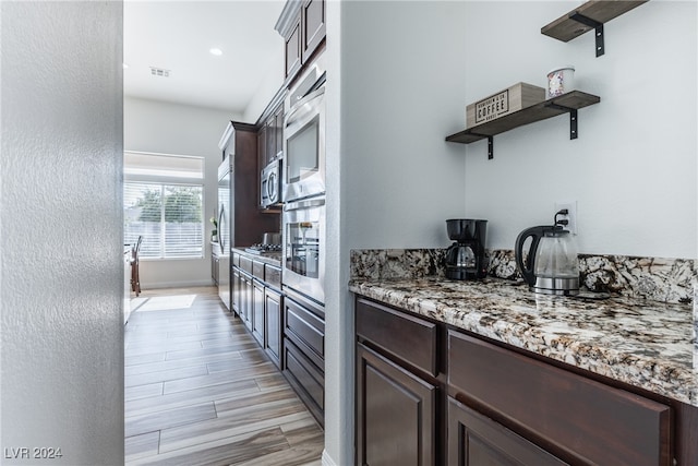 kitchen featuring light stone counters, appliances with stainless steel finishes, light wood-type flooring, and dark brown cabinets