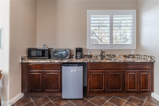 kitchen featuring light stone counters, sink, dark brown cabinetry, and dark tile patterned flooring