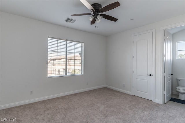 unfurnished bedroom with ensuite bathroom, light carpet, multiple windows, and ceiling fan