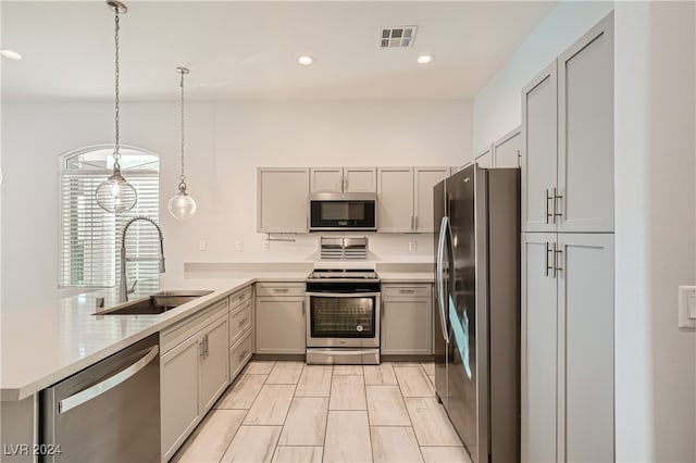 kitchen featuring kitchen peninsula, gray cabinetry, stainless steel appliances, sink, and decorative light fixtures