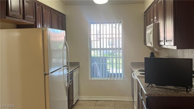 kitchen featuring light tile patterned floors, dark brown cabinets, white appliances, and stone countertops