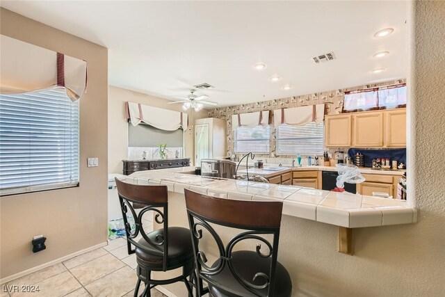 kitchen featuring light tile patterned flooring, kitchen peninsula, ceiling fan, tile counters, and a breakfast bar area