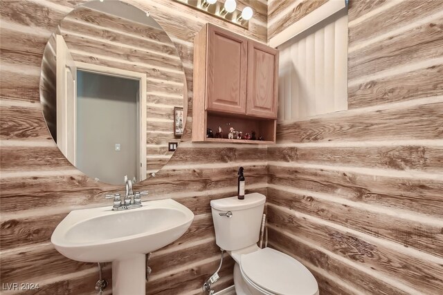 bathroom featuring toilet, sink, and rustic walls