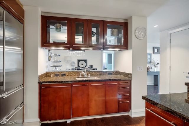 bar featuring stainless steel built in fridge, dark stone counters, sink, and dark hardwood / wood-style flooring