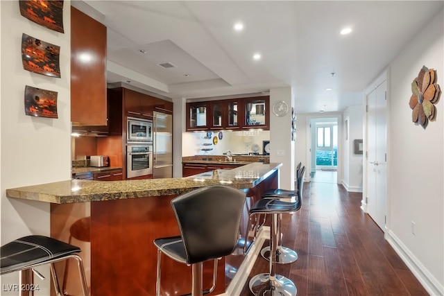 kitchen with a kitchen breakfast bar, appliances with stainless steel finishes, kitchen peninsula, and dark wood-type flooring