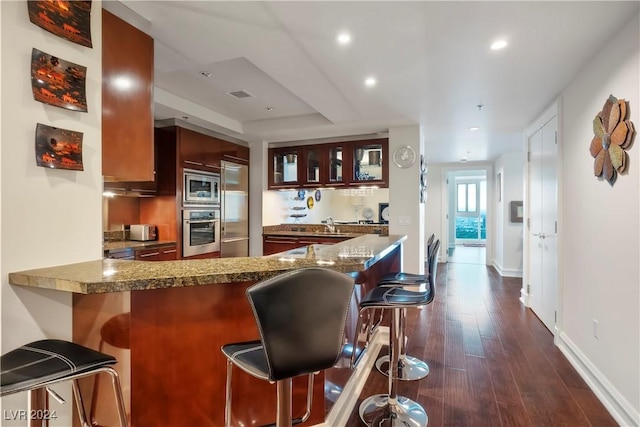kitchen with built in appliances, a kitchen breakfast bar, a peninsula, dark wood-type flooring, and glass insert cabinets