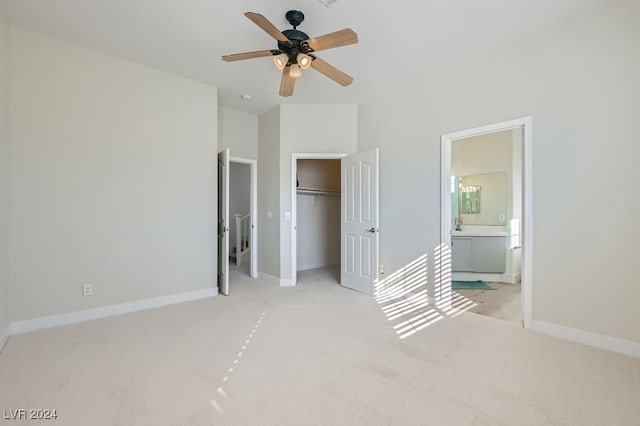 unfurnished bedroom with a closet, light colored carpet, connected bathroom, and ceiling fan