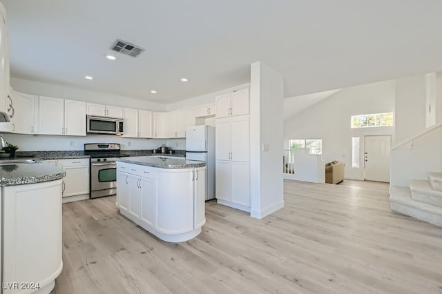 kitchen with appliances with stainless steel finishes, a center island, white cabinetry, dark stone countertops, and light hardwood / wood-style flooring