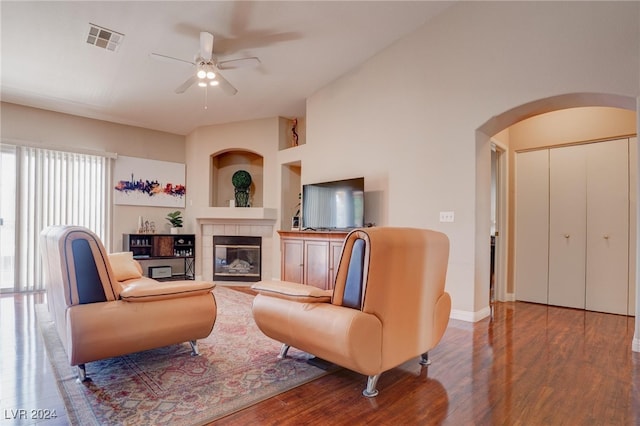 living room featuring a tiled fireplace, hardwood / wood-style floors, vaulted ceiling, built in features, and ceiling fan