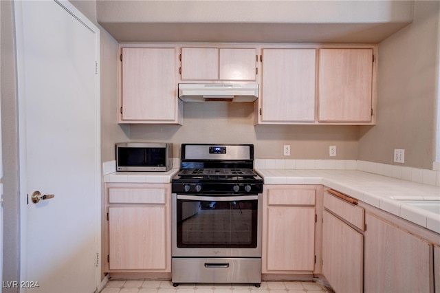 kitchen with light brown cabinetry, appliances with stainless steel finishes, and tile counters