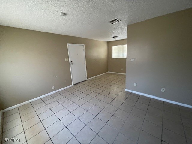 tiled empty room featuring a textured ceiling