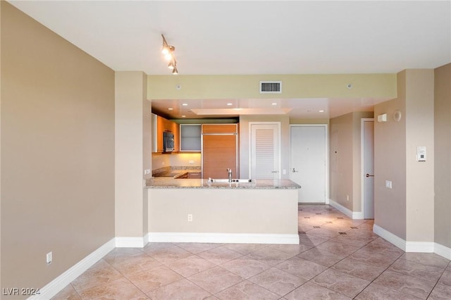 kitchen with paneled built in fridge, sink, light stone countertops, light tile patterned floors, and kitchen peninsula