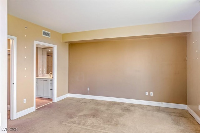 unfurnished bedroom featuring ensuite bathroom and light carpet