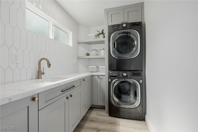 laundry area featuring sink, light hardwood / wood-style flooring, cabinets, and stacked washer and dryer