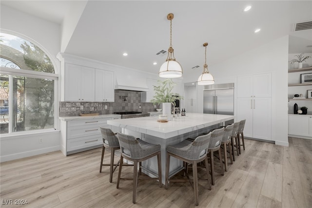 kitchen featuring a wealth of natural light, white cabinets, a kitchen island with sink, and light wood-type flooring